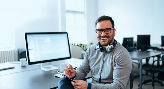 Stets an Ihrer Seite – Unser Engagement für eine dauerhaft starke Webpräsenz. Freundlicher Kundensupport-Mitarbeiter mit Headset vor einem Computerbildschirm, symbolisiert dauerhafte Kundenbetreuung und Website-Optimierung.