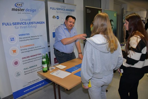Mitarbeiter von master design erklärt interessierten Schülerinnen das Leistungsangebot des Unternehmens am Karrieretag 2025.