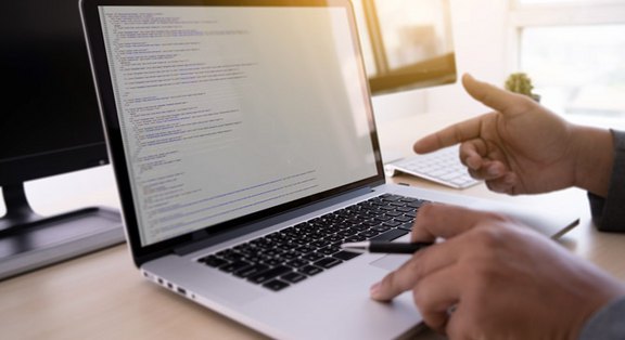Hinter den Kulissen – Unsere Profis programmieren den Erfolg Ihrer Webseite. Hände auf einem Laptop, der Programmiercode zeigt, symbolisieren professionelle Website-Optimierung und Wartung